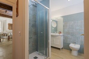 Ein modernes Badezimmer mit einer in Glas abgeschlossenen Dusche, einem Waschbecken mit Bidet und einem Spiegel mit rundem Rahmen.