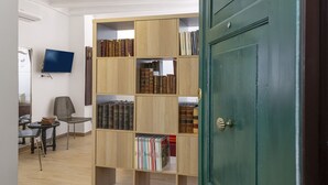 A room with a wooden bookshelf filled with books, a television mounted on the wall, and a green door. - Banchi Prestige - Castel Sant'Angelo (Roma)