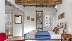 A bedroom with a bed, a red chair, a wooden table, and a window with a view of buildings. - Banchi Prestige - Castel Sant'Angelo (Roma)