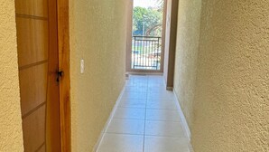 A narrow hallway with a wooden door on the left and a view of a balcony with a railing. - Cozy house in Polvilho Cajamar, just a few minutes from Rod. Anhanguera (Jardim Santana Cajamar)