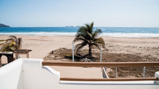 Vista de platja amb una palmera i un edifici blanc al primer pla.
