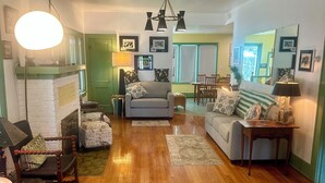 A spacious living room with a fireplace, wooden flooring, and a dining area in the background. - Spacious Vintage Getaway. Walkable! (Casper)