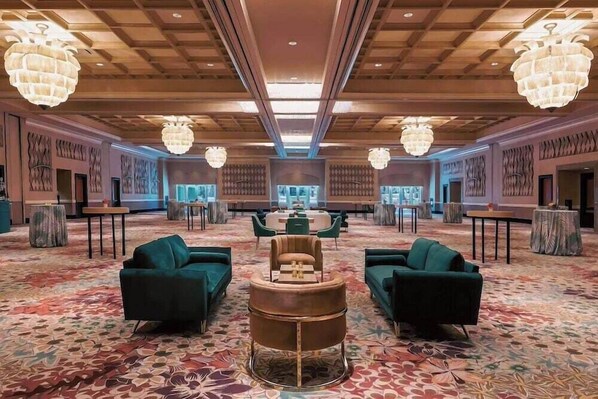 Un hall d’entrée spacieux, doté d’un tapis à motifs, de canapés verts, d’une table ronde centrale et de grands lustres.