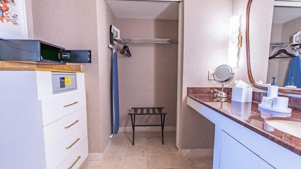 Un baño con lavamanos, espejo, toallero y un pequeño banco.