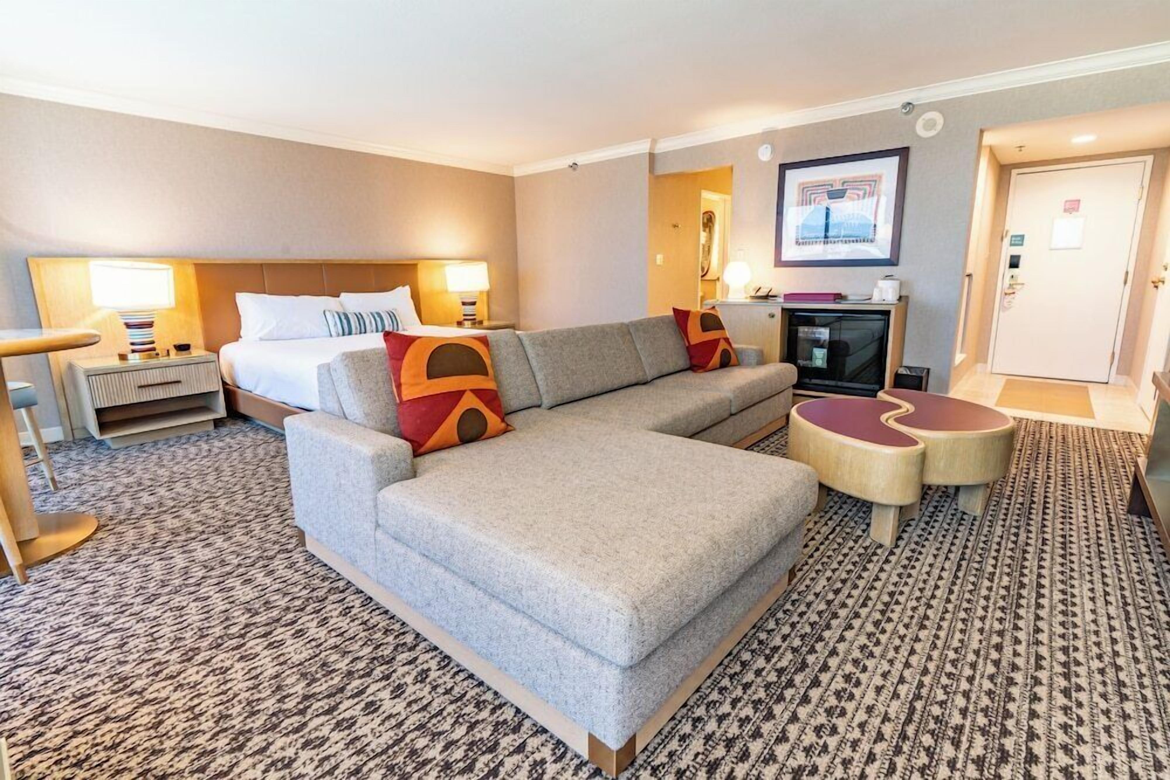 A hotel room with a sofa, a bed, a desk, and a patterned carpet.