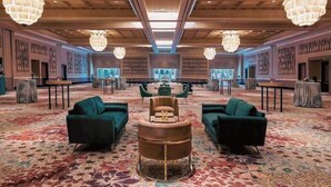Eine geräumige Lobby mit Teppichmuster, grünen Sofas, einem runden Tisch in der Mitte und großen Kronleuchtern.