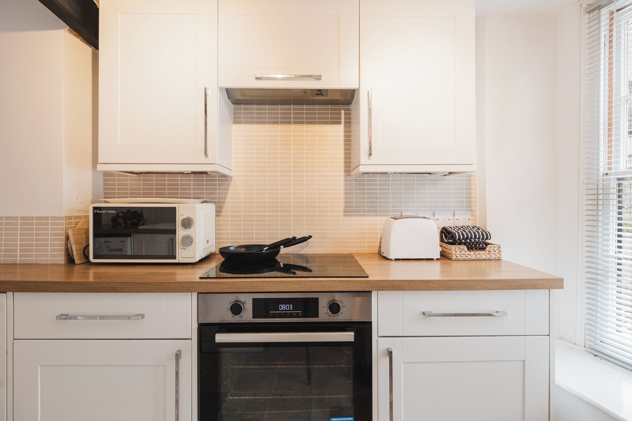 A modern kitchen with white cabinets, a microwave, a toaster, and a stove.