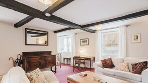 Ett mysigt vardagsrum med ett träbord, en vit soffa och en träbyrå. Där finns också ett skrivbord med en lampa och en stol, samt ett fönster med gardiner.