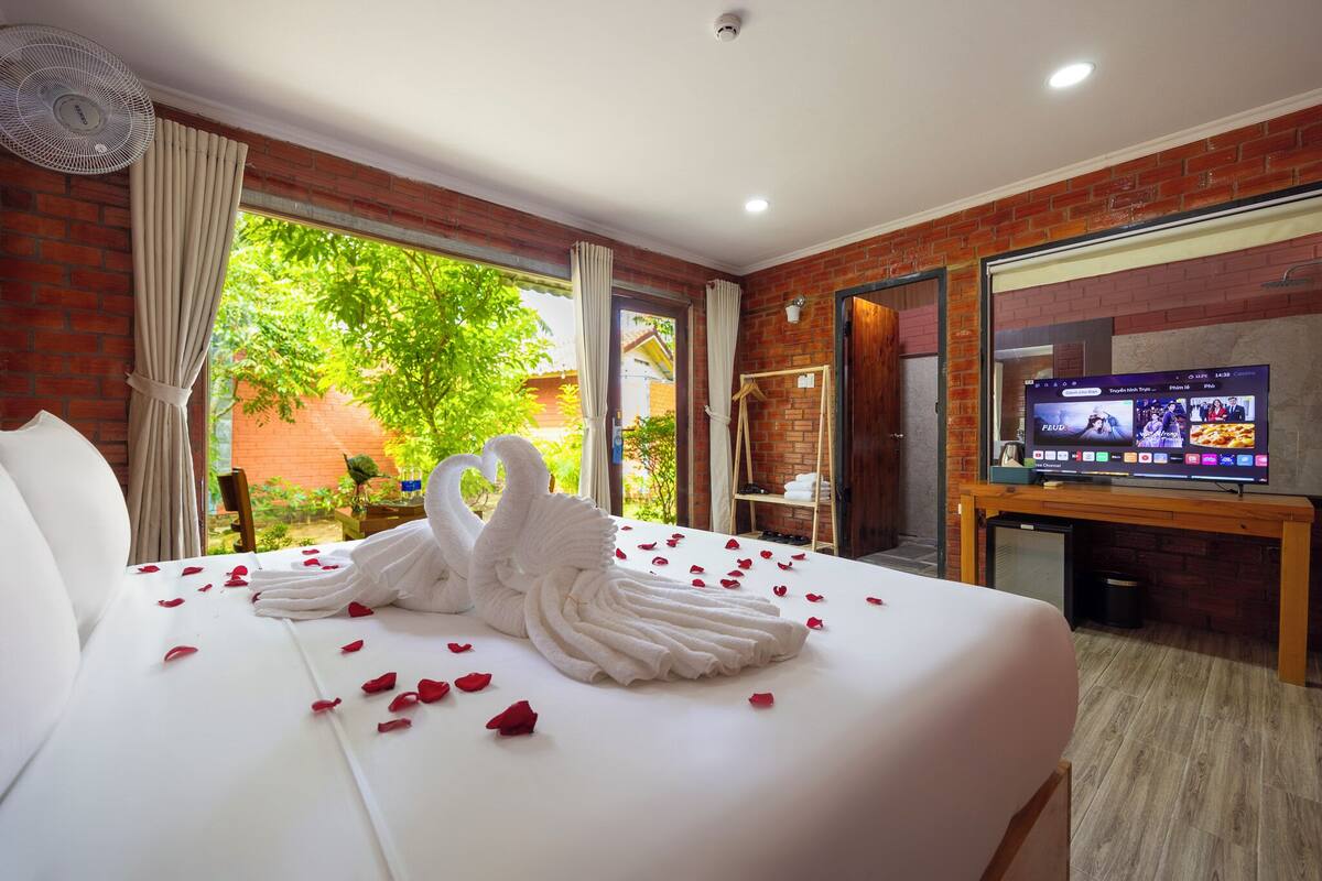 A hotel room with a bed, a TV, and a view of greenery outside.