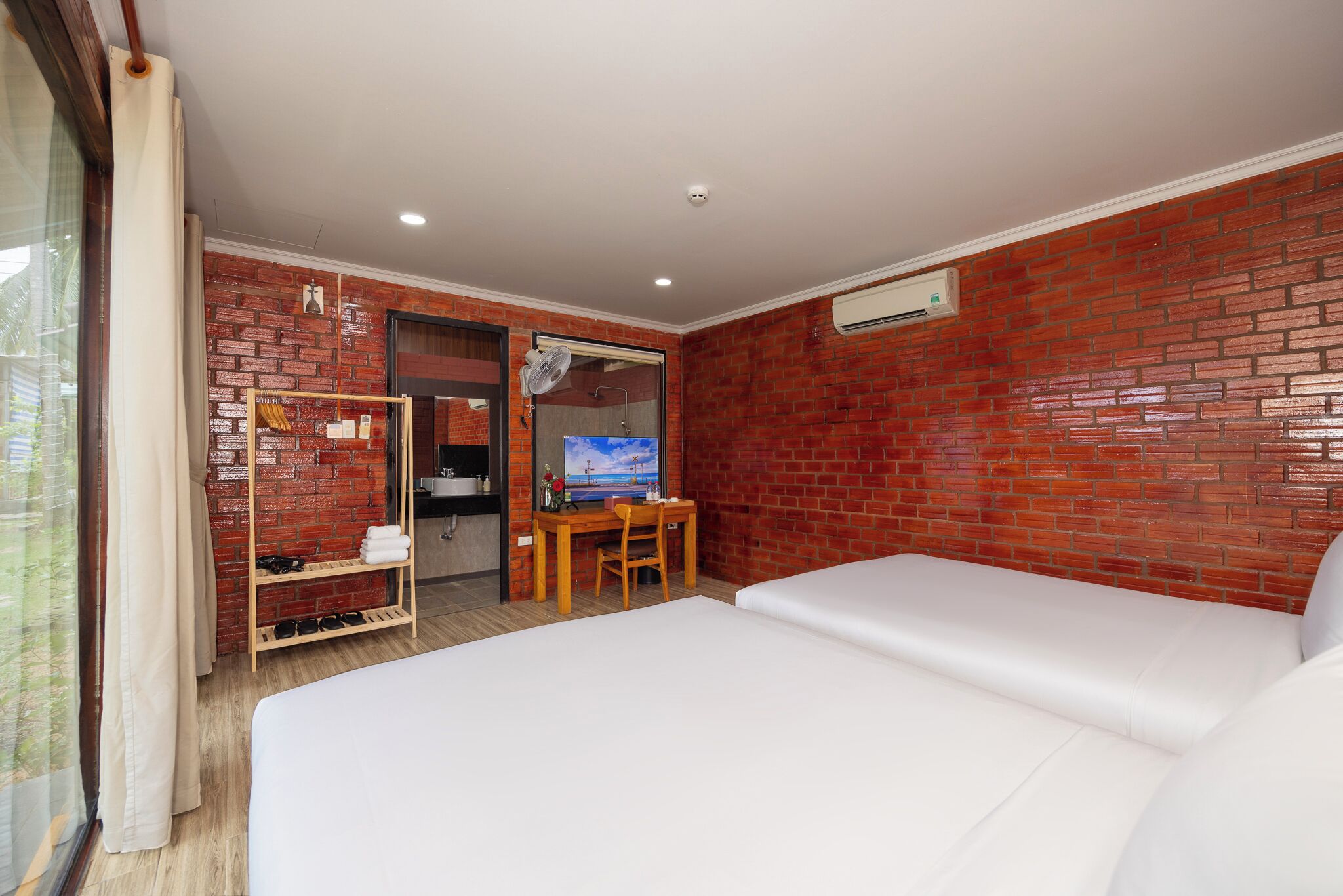 Habitación de hotel con pared de ladrillo, una cama, un escritorio con silla y un televisor.