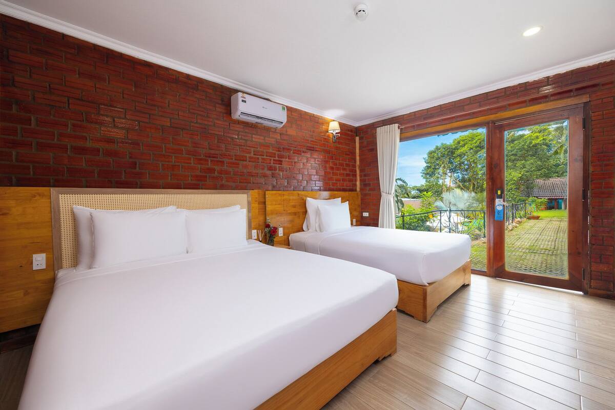A hotel room with two beds, a brick wall, and a view of a garden.