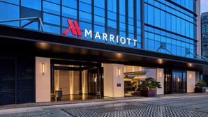 Entrada de um hotel Marriott com fachada de vidro, sinalização iluminada e plantas em vasos.