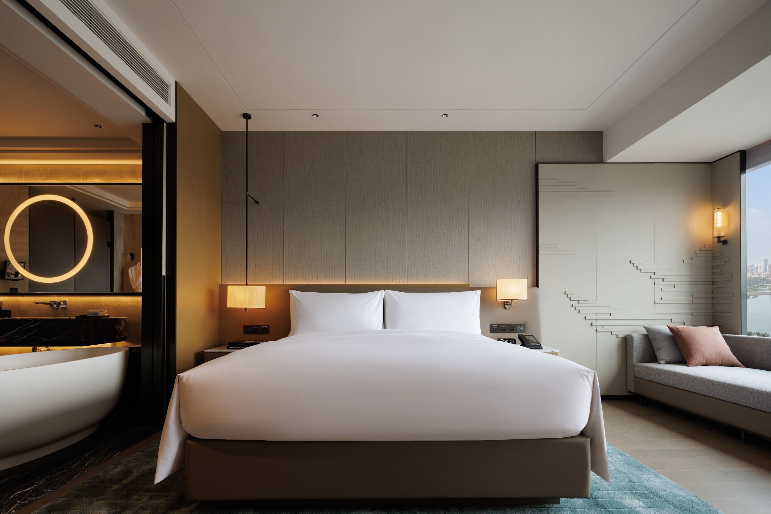 A modern hotel room with a large bed, a built-in bathtub, a seating area with a view, and a staircase.