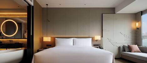 A modern hotel room with a large bed, a built-in bathtub, a seating area with a view, and a staircase.