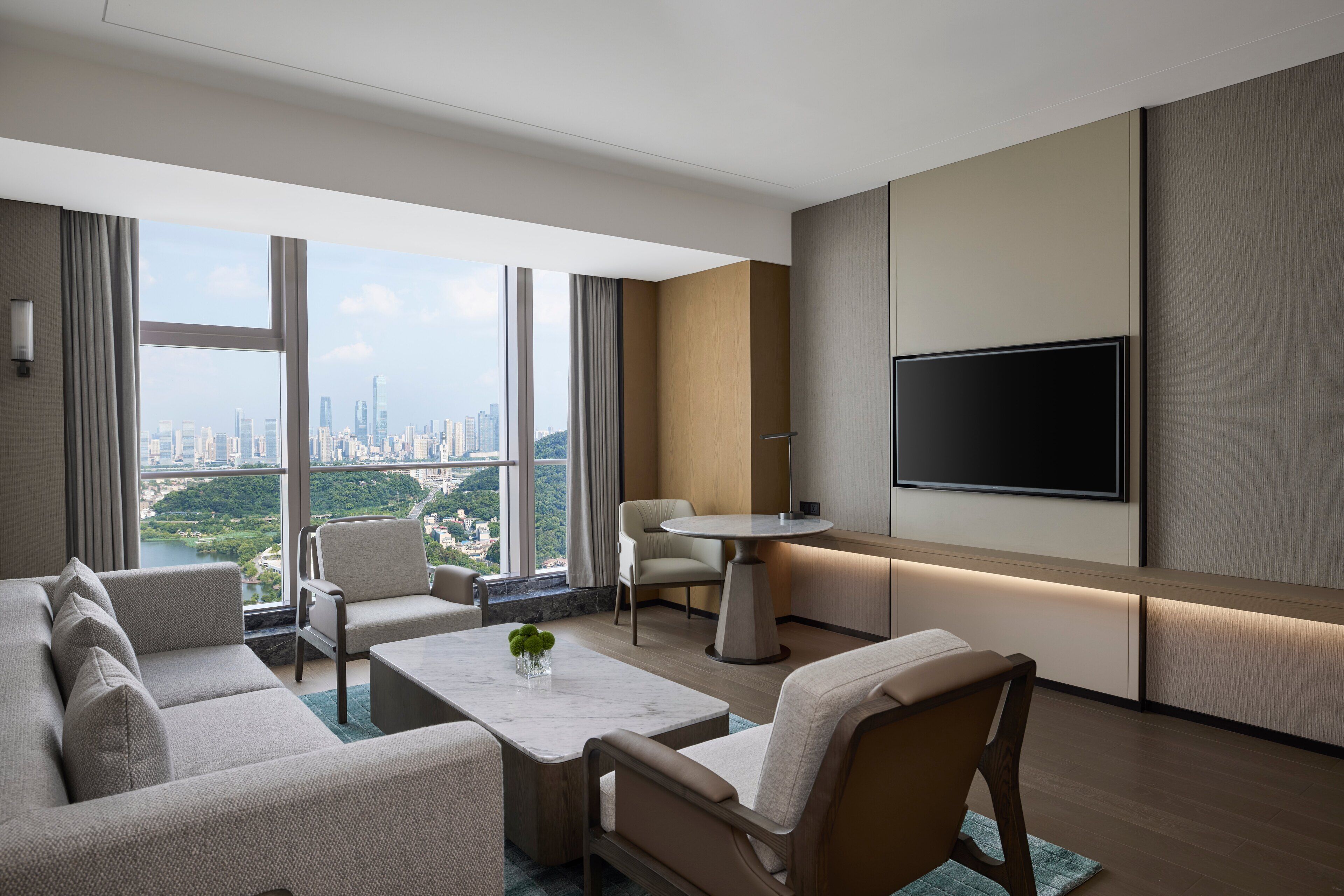 A modern hotel room with a city view, a flat-screen TV, and a cozy seating area.