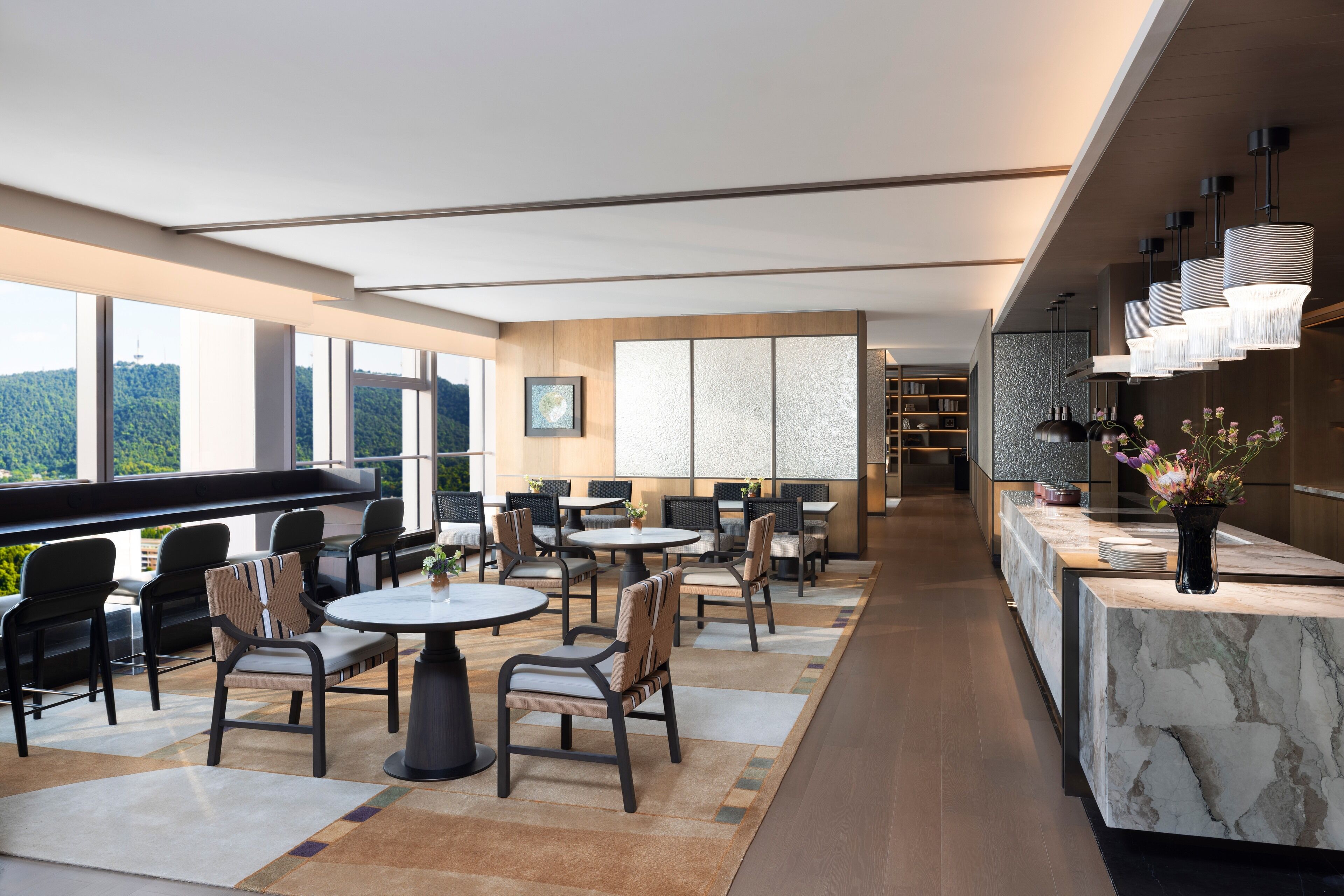 Un comedor moderno con mesas y sillas redondas, una encimera de mármol y ventanas amplias que ofrecen vistas al exterior.