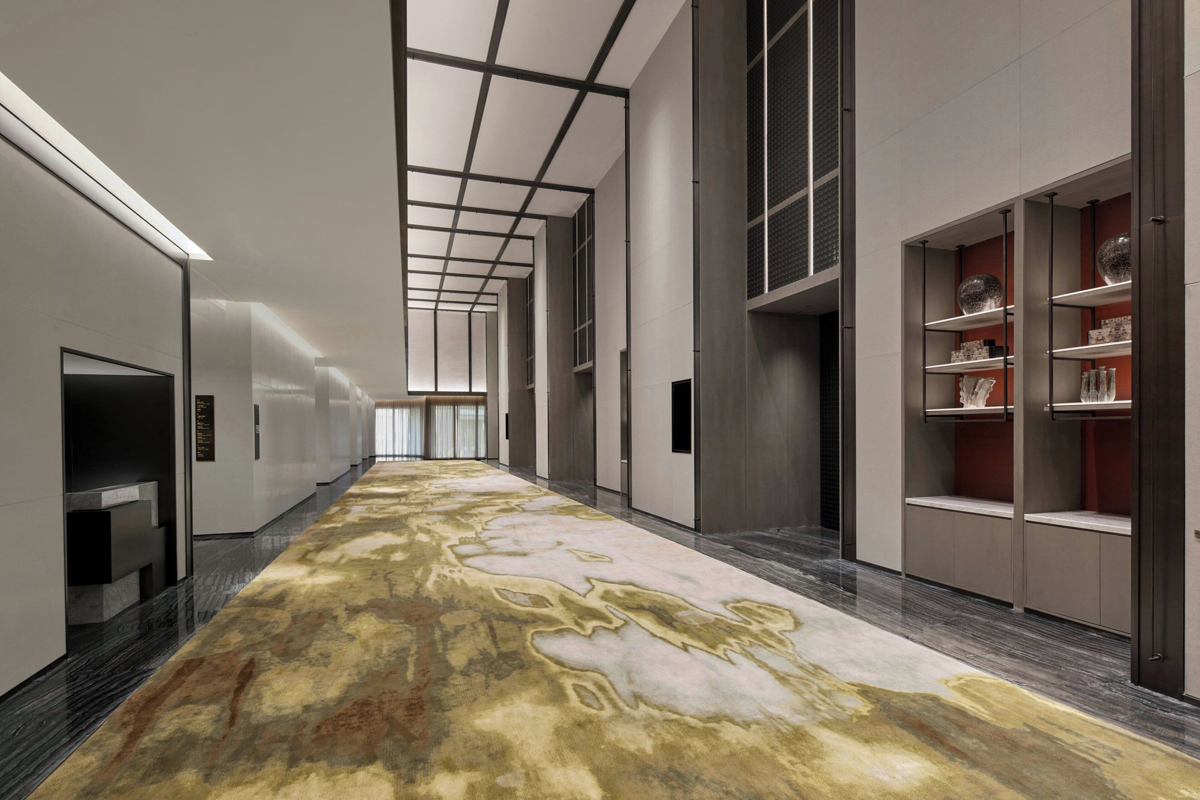 A modern hotel corridor with a patterned carpet, built-in shelves, and a long hallway.