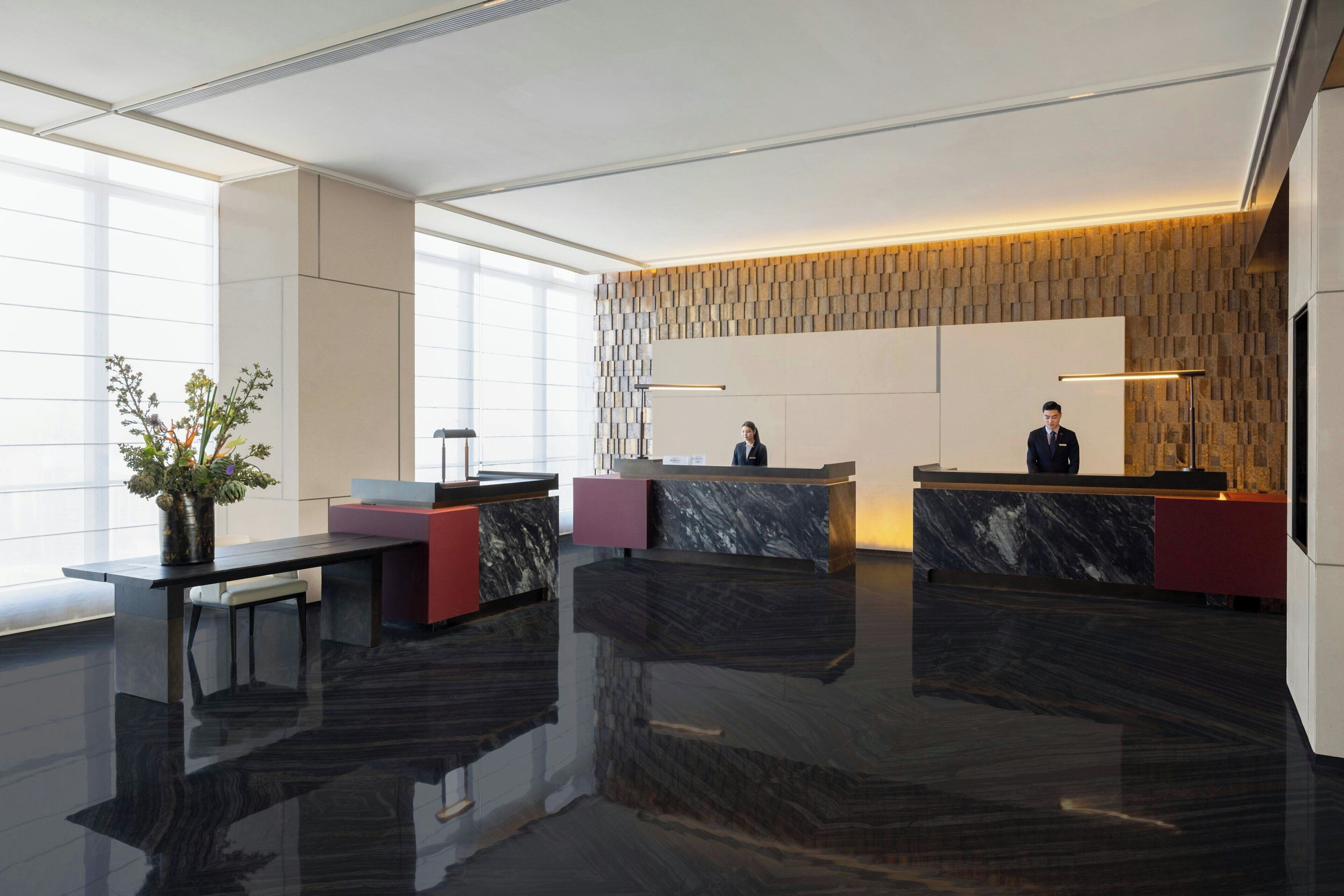 Un área de recepción moderna con mostradores de mármol, una planta grande en maceta y un revestimiento de pared con diseño.