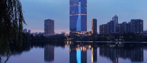 A high-rise hotel with a modern design, situated by a calm body of water, reflecting the building and the surrounding cityscape.