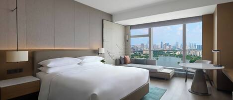 Una habitación de hotel moderna con una cama grande, una zona de estar, una mesa de comedor y vistas a la ciudad.