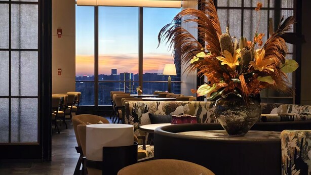Um salão moderno com uma grande janela que oferece vista da cidade ao pôr do sol.