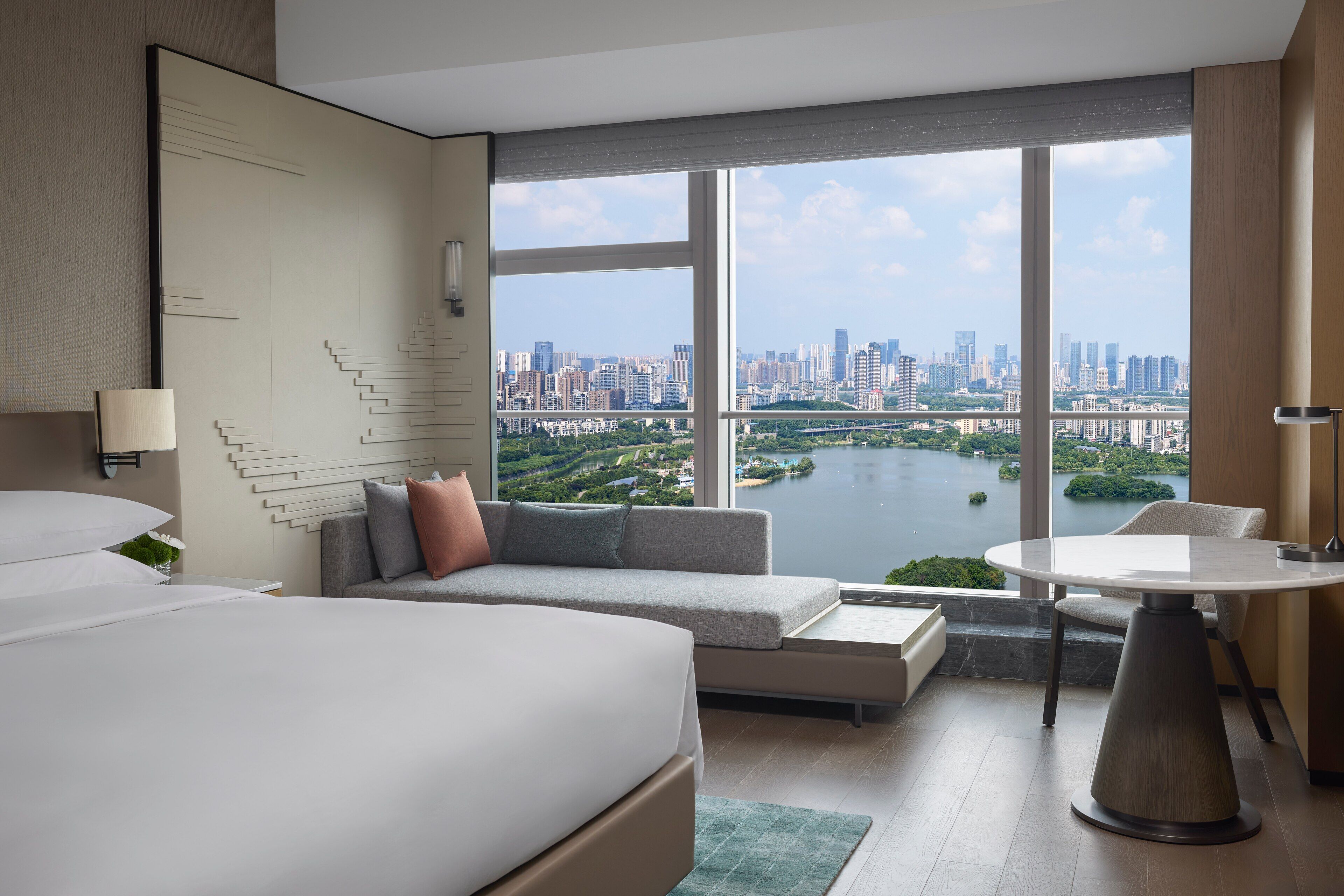 Habitación de hotel moderna con una cama grande, un sofá, una mesa de comedor y vistas a la ciudad y al agua.