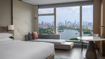Habitación de hotel moderna con una cama grande, un sofá, una mesa de comedor y vistas a la ciudad y al agua.