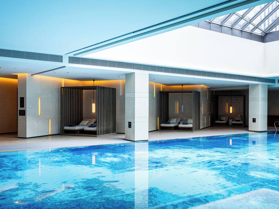 Een modern binnenzwembad met loungegedeeltes en een dakraam.