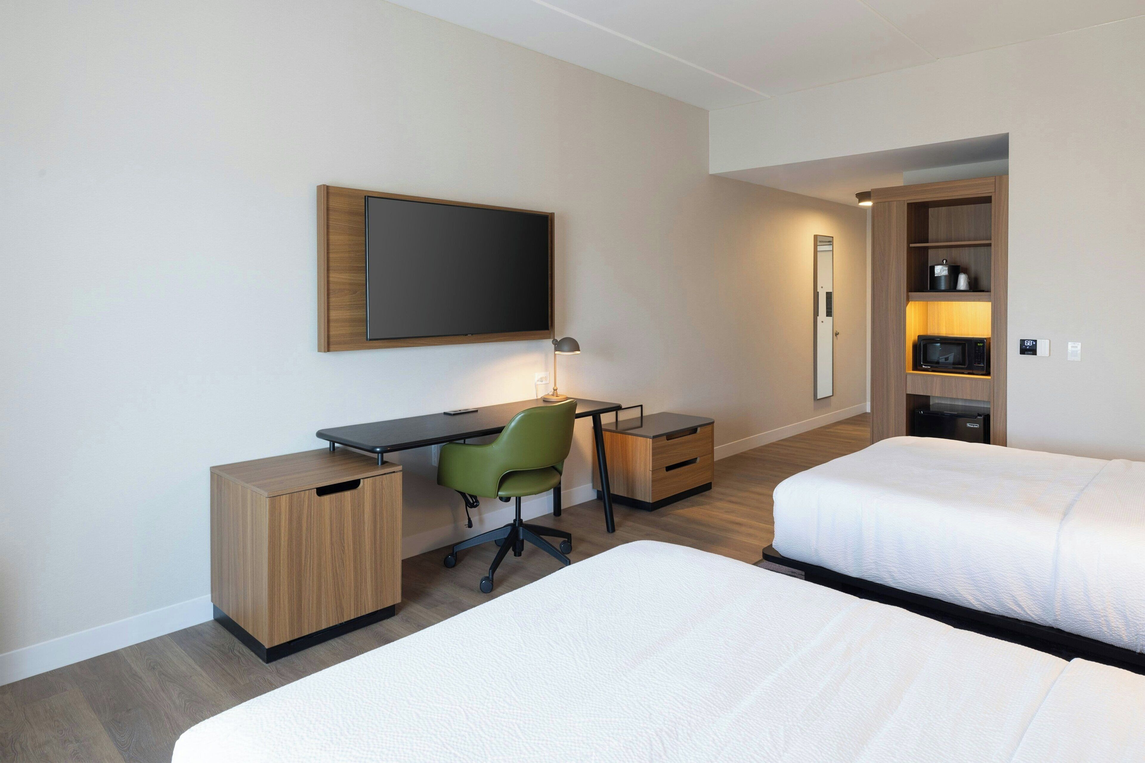 A hotel room with a desk, a green chair, a bed, and a wardrobe.