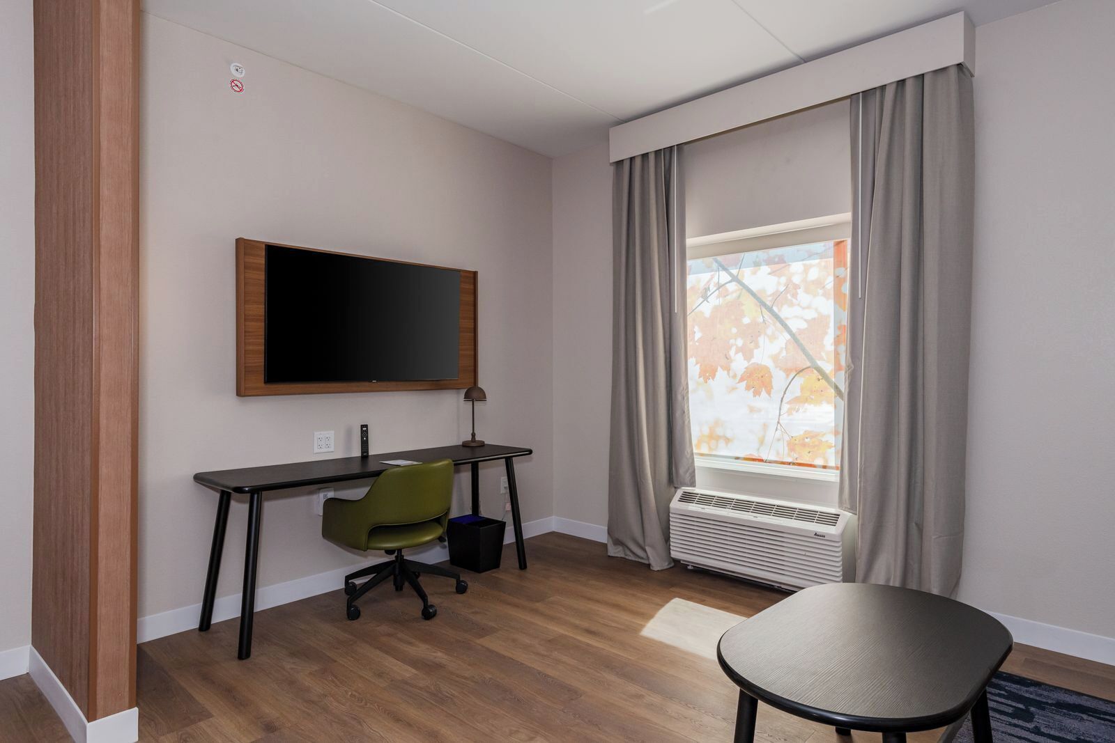 A hotel room with a desk, chair, and a large window with curtains.