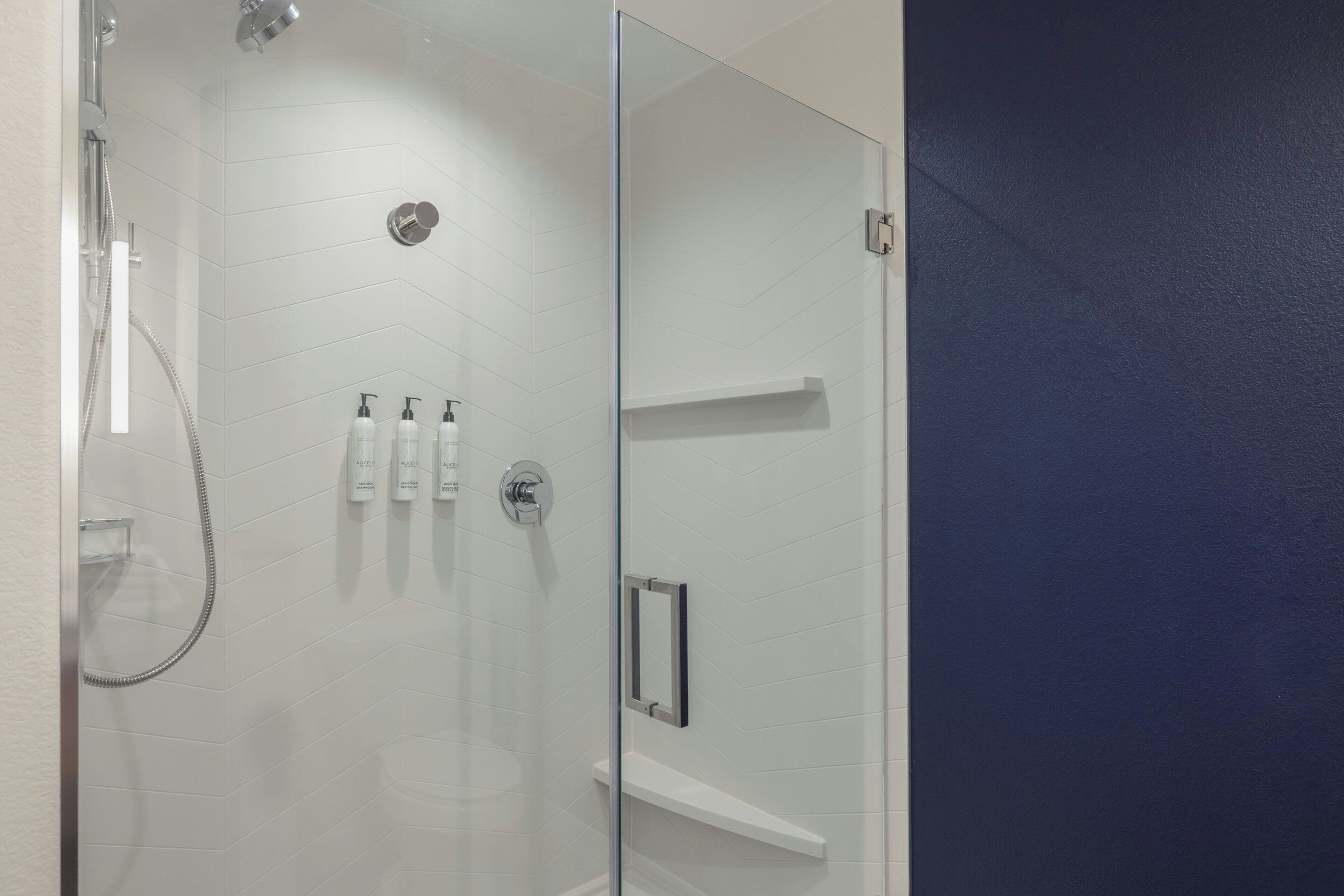 A modern bathroom with a glass shower enclosure, white tiled walls, and a built-in shelf with toiletries.