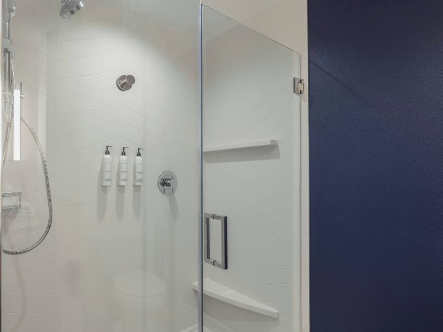 A modern bathroom with a glass shower enclosure, white tiled walls, and a built-in shelf with toiletries.