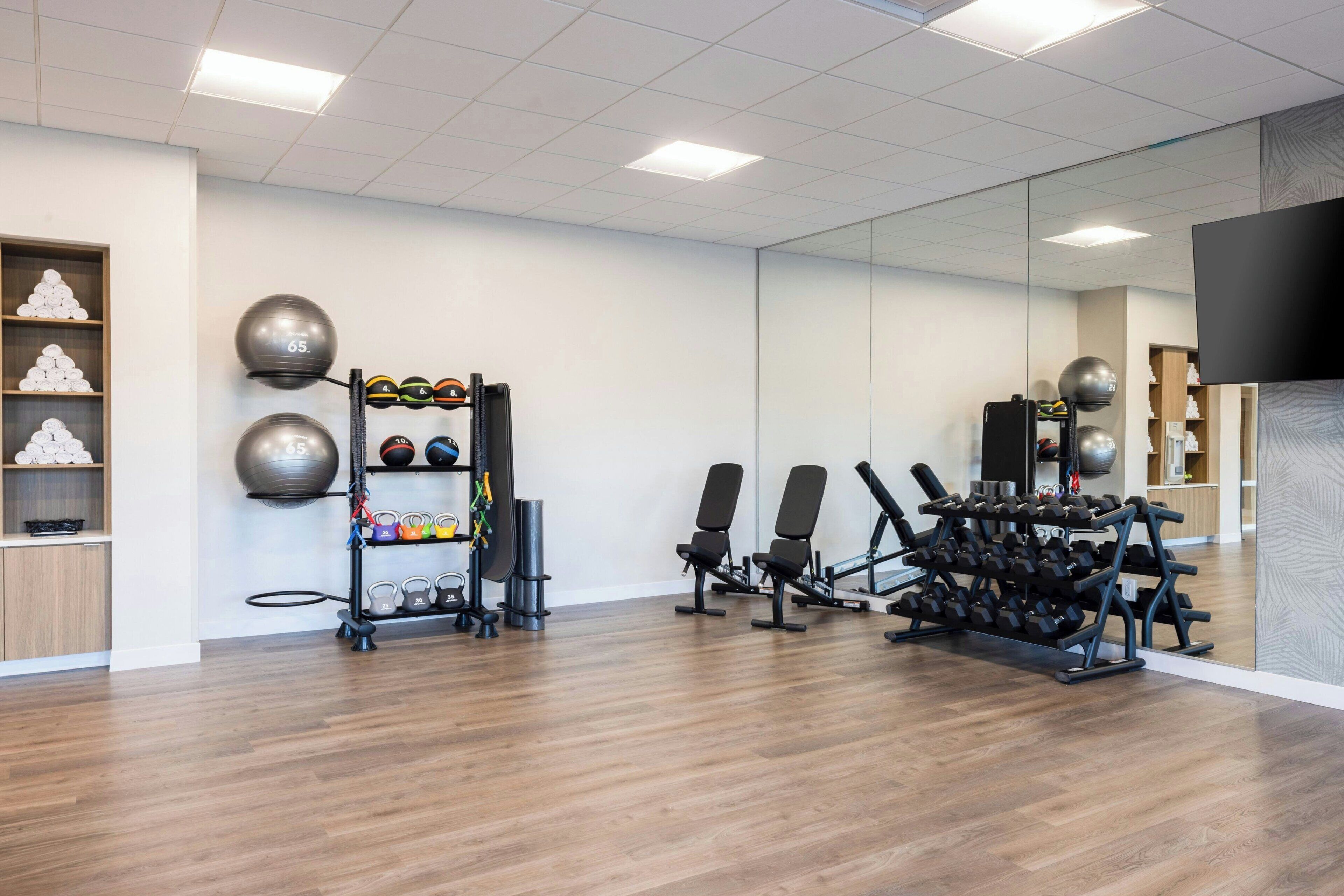 Un gimnasio moderno con suelo de madera, equipamiento de ejercicio y paredes con espejos.