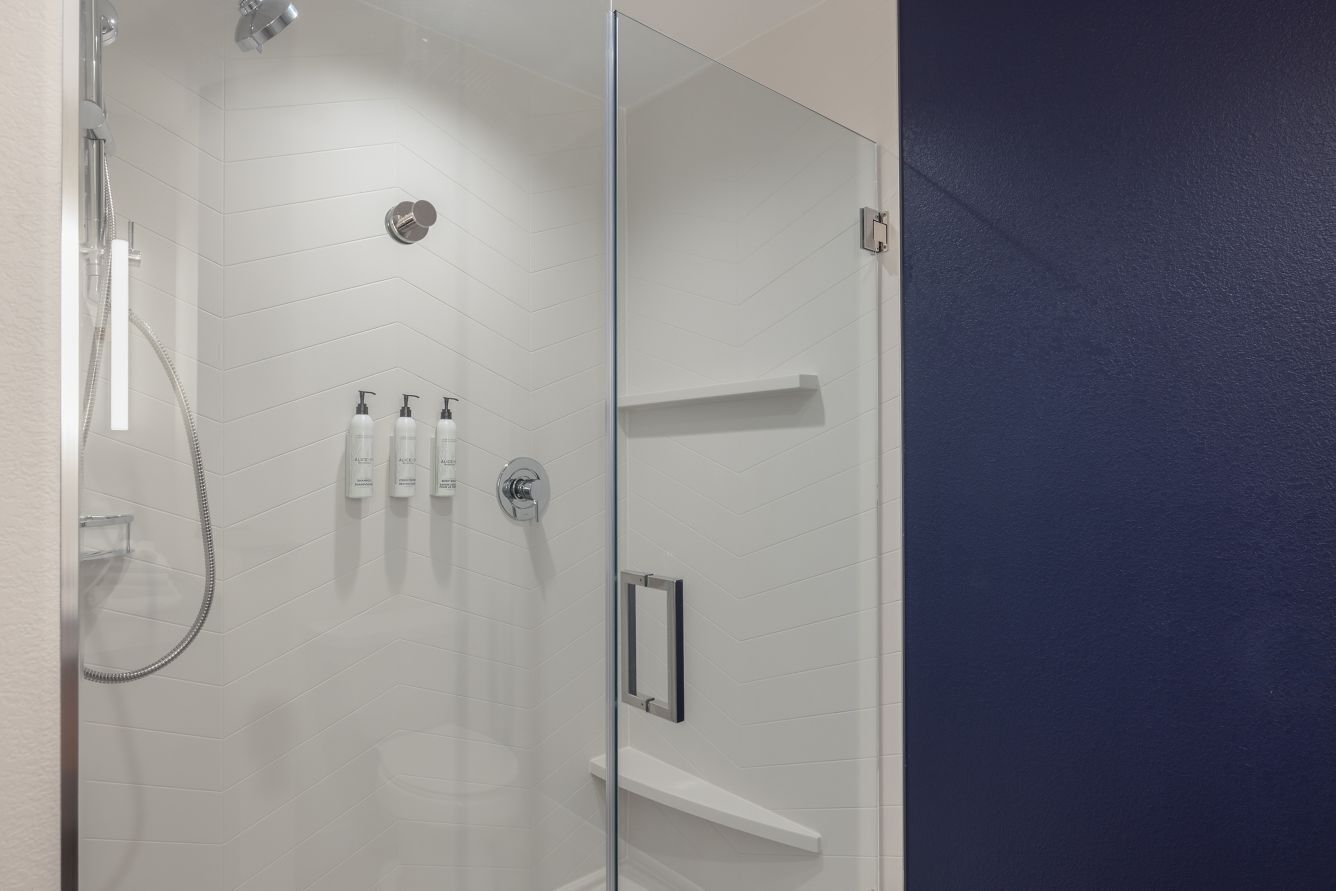 A modern shower area with a glass door, a handheld showerhead, and a wall-mounted faucet.