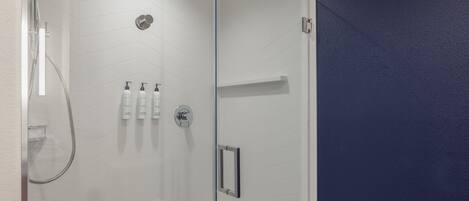Un área de ducha moderna con puerta de vidrio, cabezal de ducha de mano y grifo empotrado.