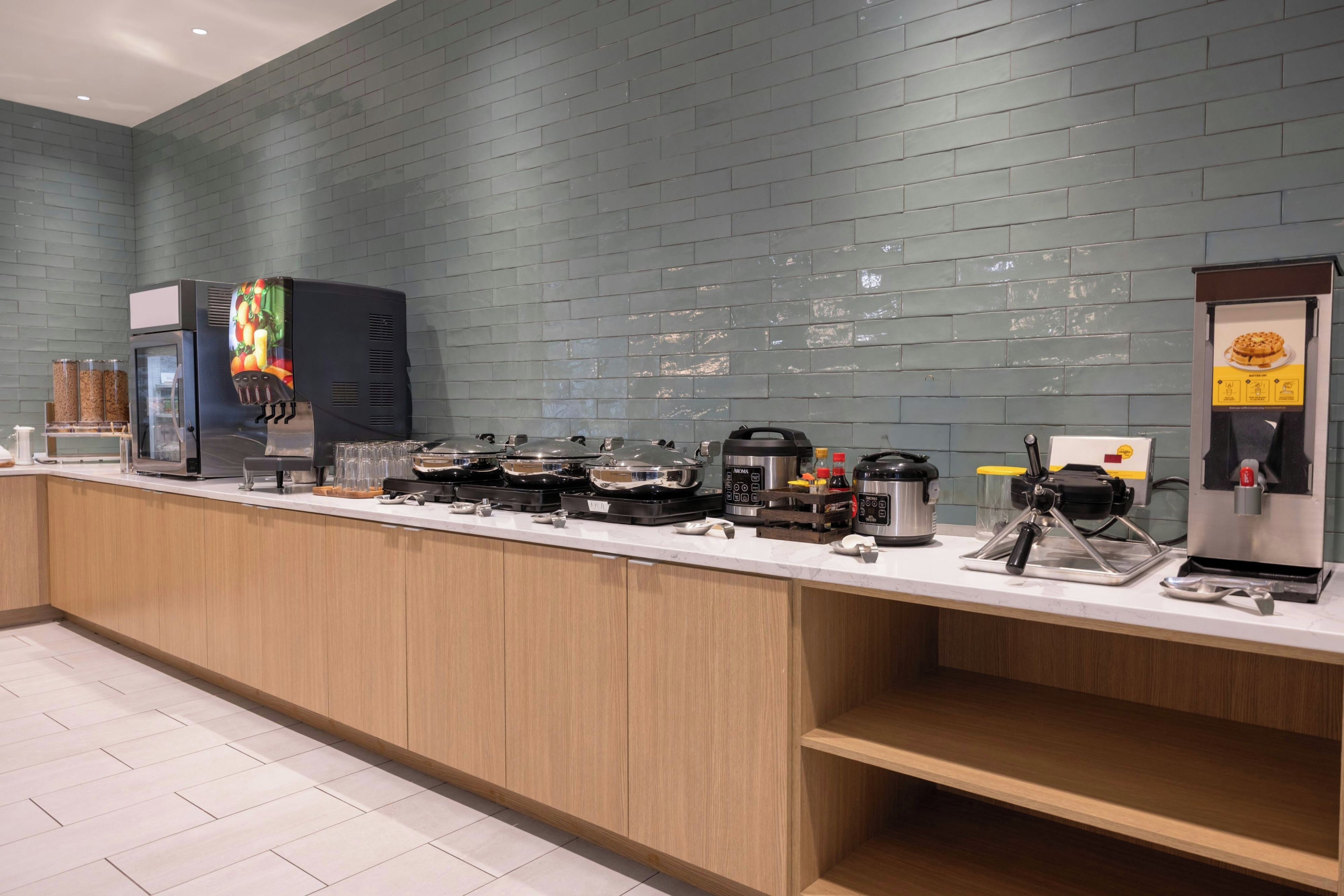 A self-service breakfast bar with various food preparation stations, including a coffee machine and a food display.