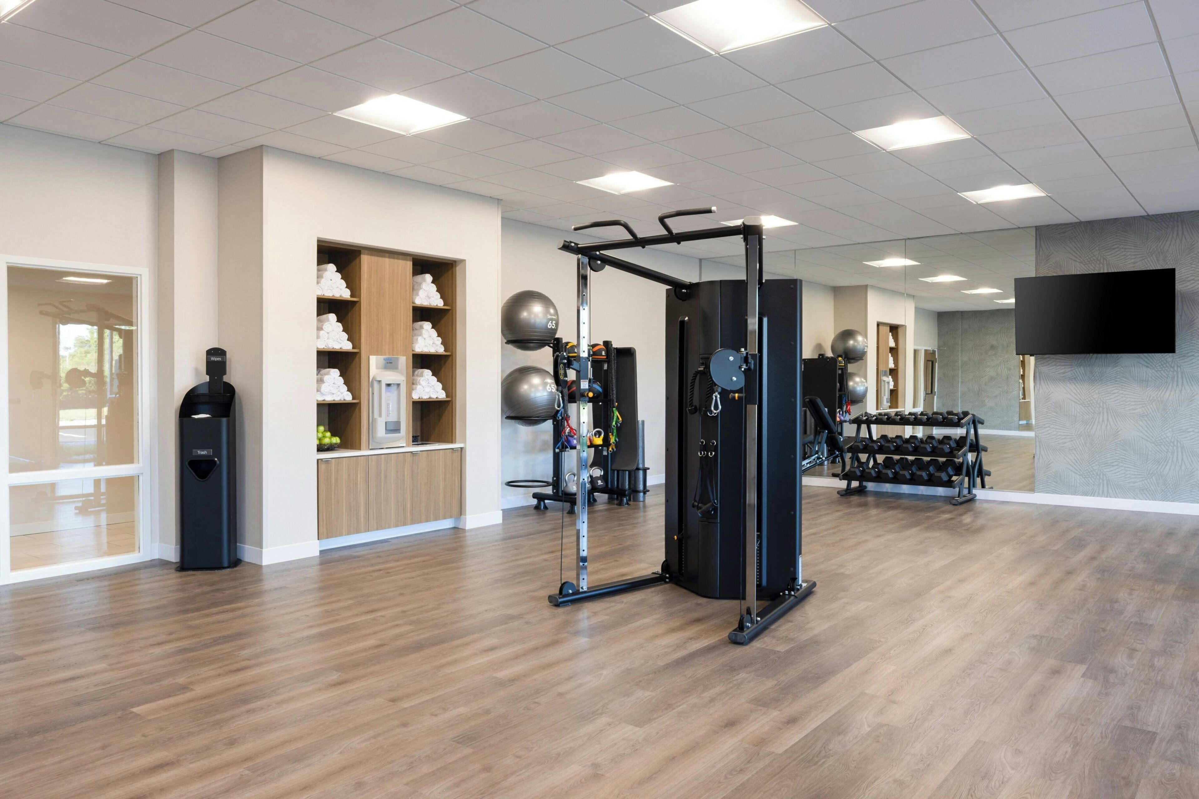 A modern gym with exercise equipment, a wall-mounted TV, and a wooden floor.