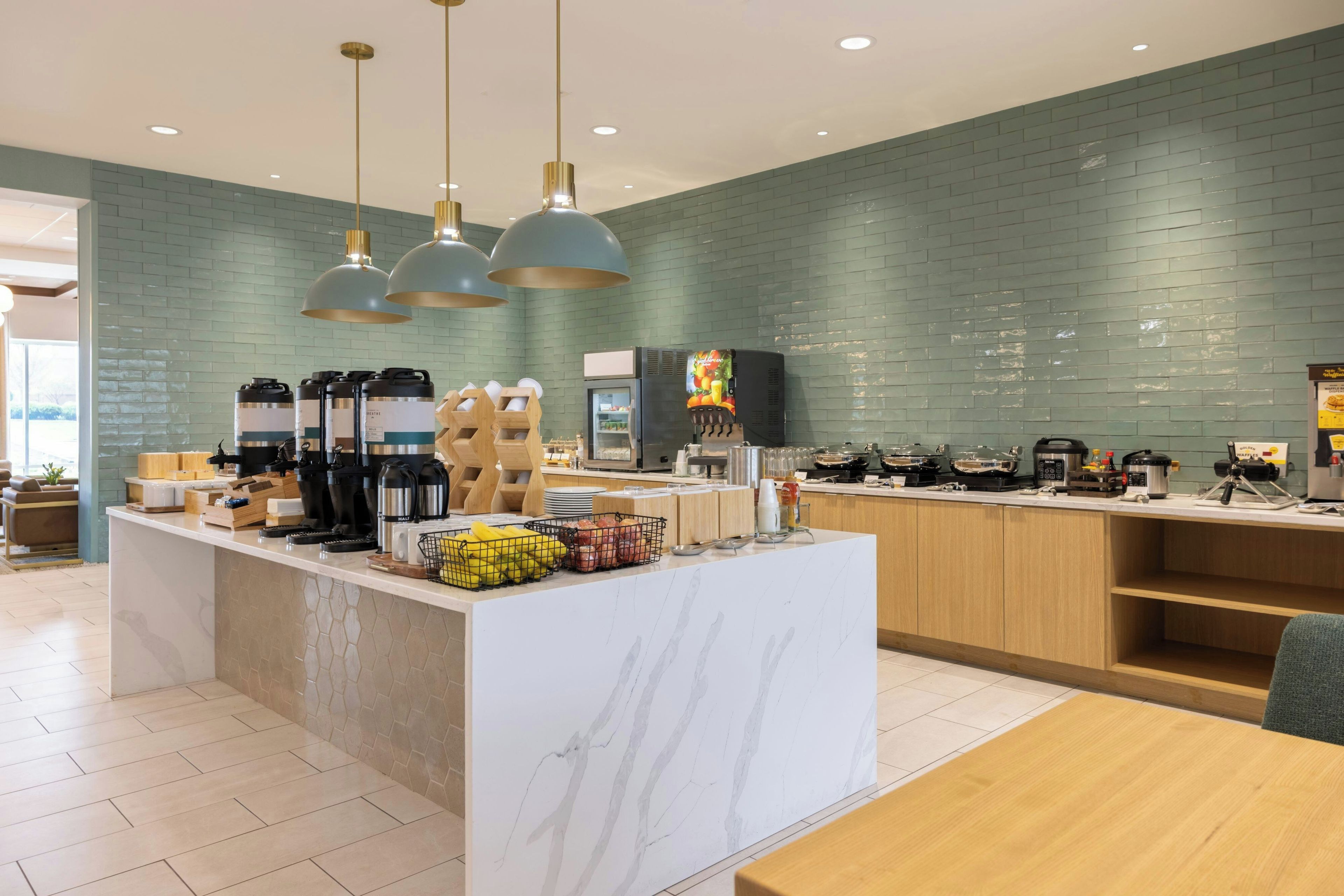 A modern kitchen area with a marble countertop, a coffee station, and a fruit display.