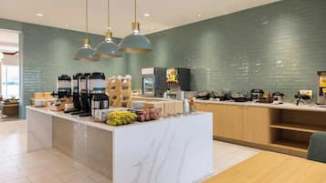 A modern kitchen area with a marble countertop, a coffee station, and a fruit display.