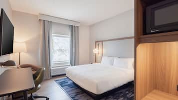 Une chambre d’hôtel avec un lit, un bureau, une chaise, une télévision et une fenêtre avec des rideaux.