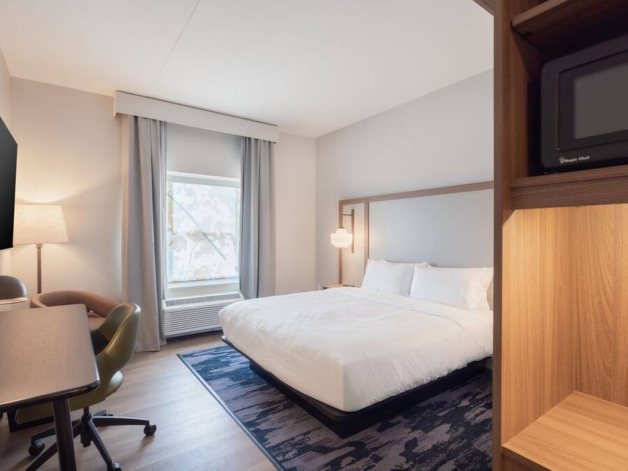 A hotel room with a bed, a desk, a chair, a TV, and a window with curtains.