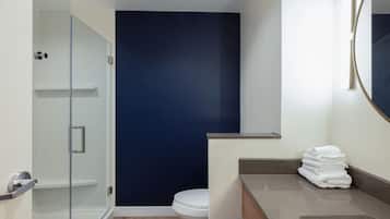 Un baño moderno con cabina de ducha de vidrio, inodoro blanco y tocador con espejo y una pila de toallas.