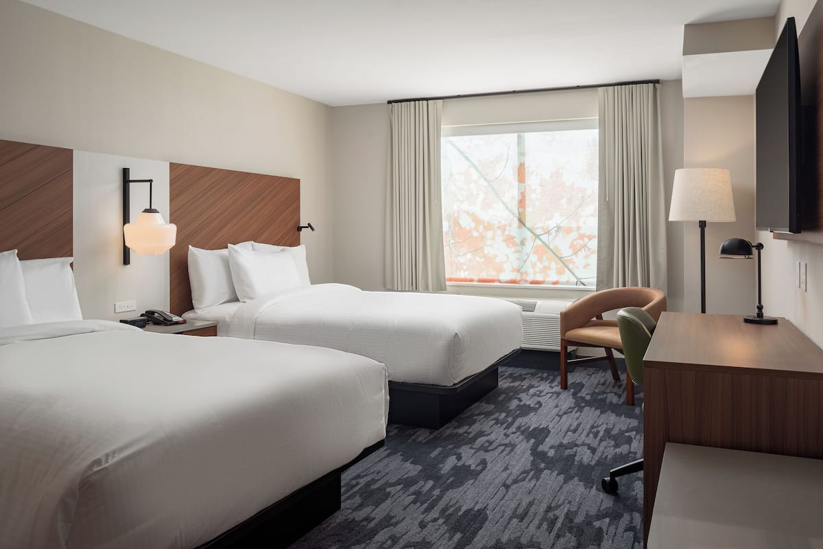 A hotel room with two beds, a desk, a chair, a TV, and a window with curtains.