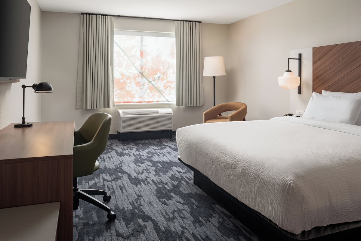 A hotel room with a bed, a desk, a chair, a TV, a lamp, and a window with curtains.