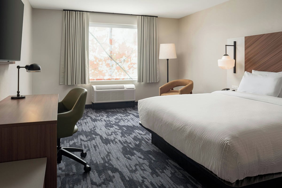A hotel room with a large bed, a desk, a chair, a lamp, and a window with curtains.