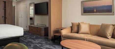 A hotel room with a bed, a sofa, a small table, a TV, a mirror, and a painting on the wall.