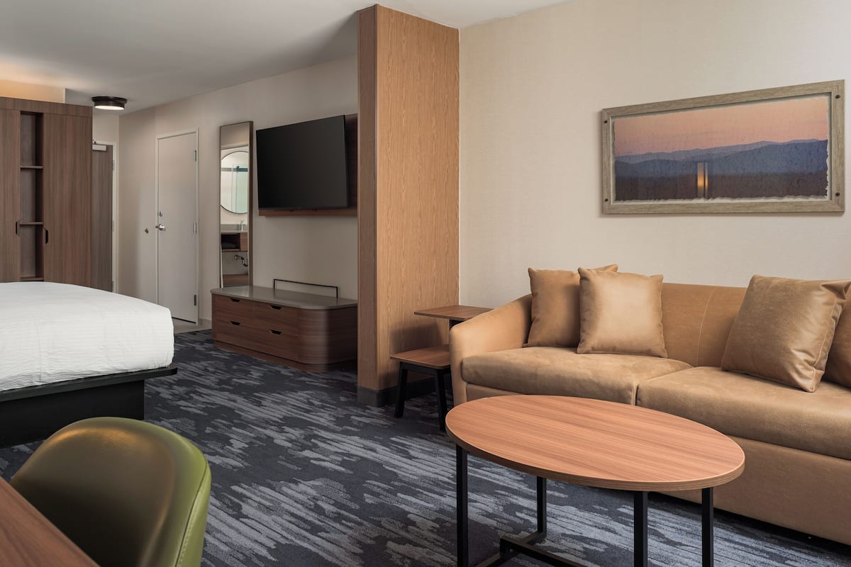A hotel room with a bed, a sofa, a small table, a TV, and a painting on the wall.