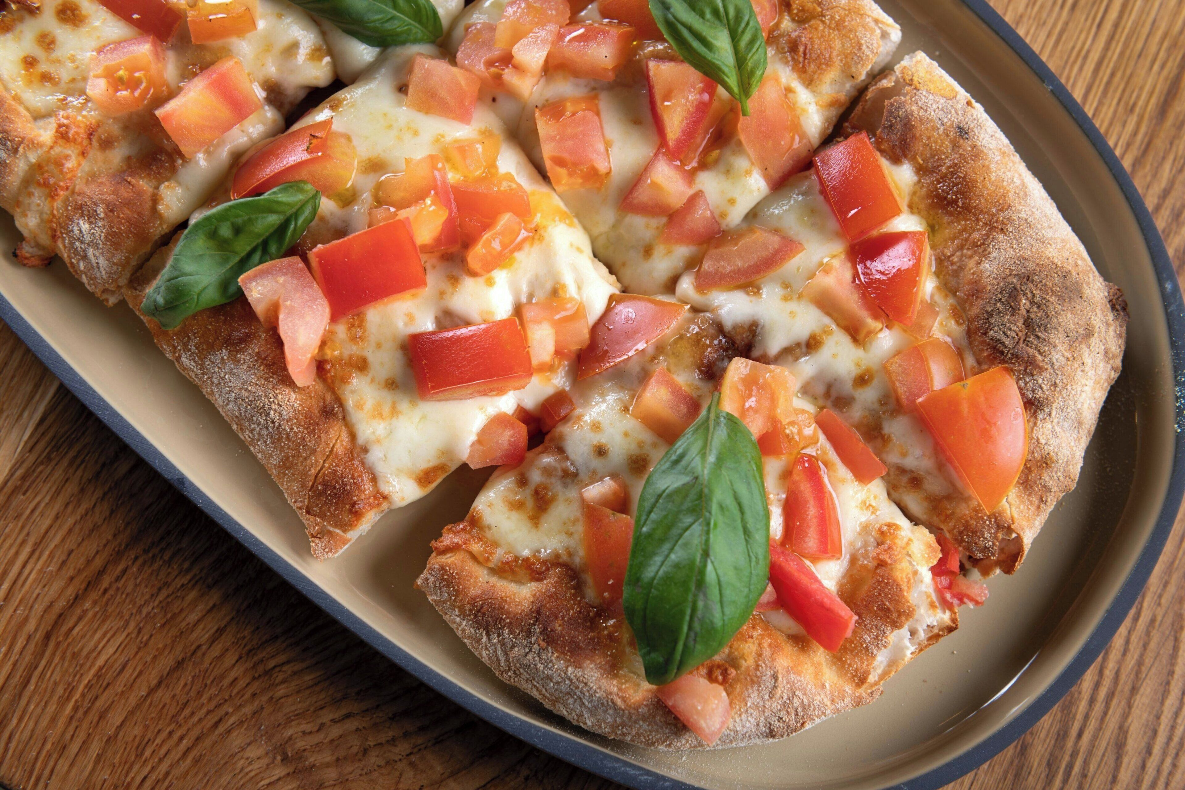 A rectangular serving dish containing a pizza with tomato and basil toppings.