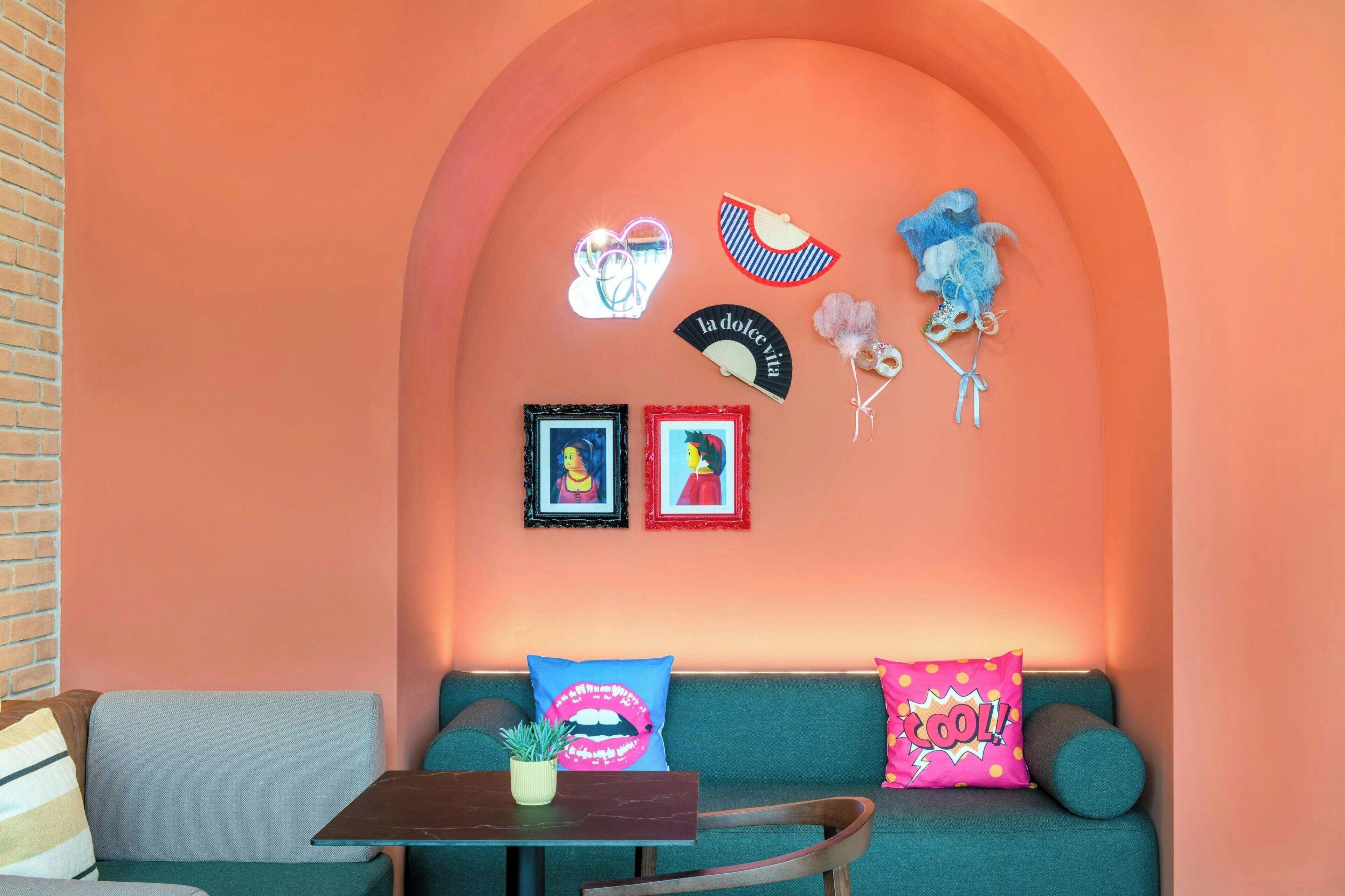 A cozy seating area with a teal sofa, a small table with a plant, and a wall adorned with framed artwork and decorative items.