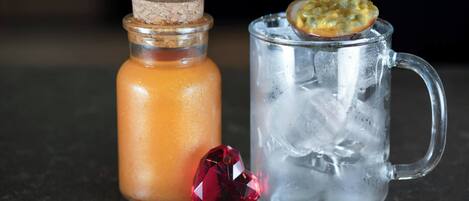 A clear glass mug with ice and a slice of passion fruit on top, next to a glass bottle with a cork stopper.